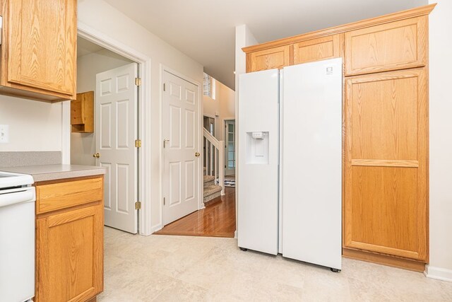 kitchen with white fridge with ice dispenser, range, light countertops, and light brown cabinetry