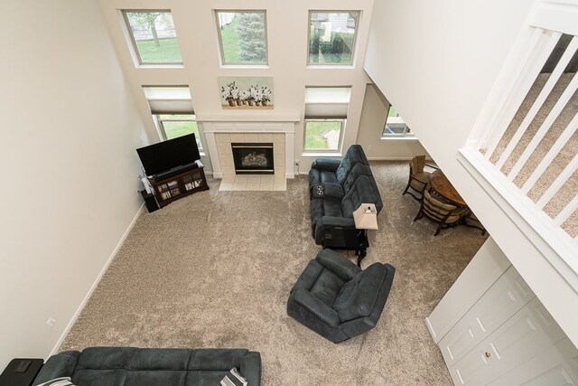 carpeted living room with a tiled fireplace, a towering ceiling, and baseboards