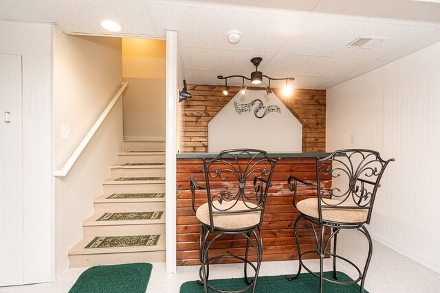 dining area with a paneled ceiling, wooden walls, and stairs