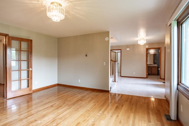 spare room with a chandelier, light wood-style floors, healthy amount of natural light, and baseboards