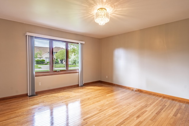 empty room with a chandelier, light wood-type flooring, and baseboards