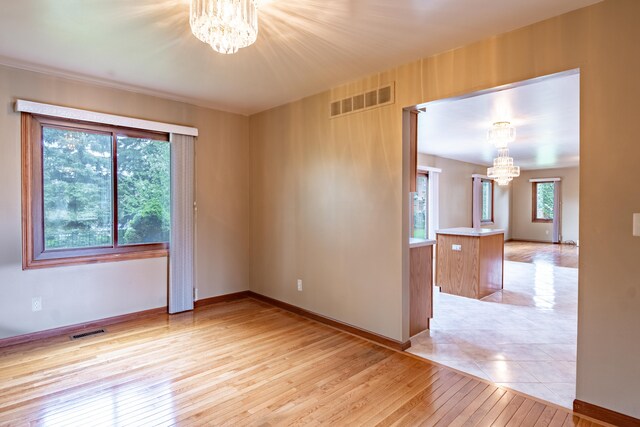 spare room featuring a chandelier, light wood finished floors, and baseboards