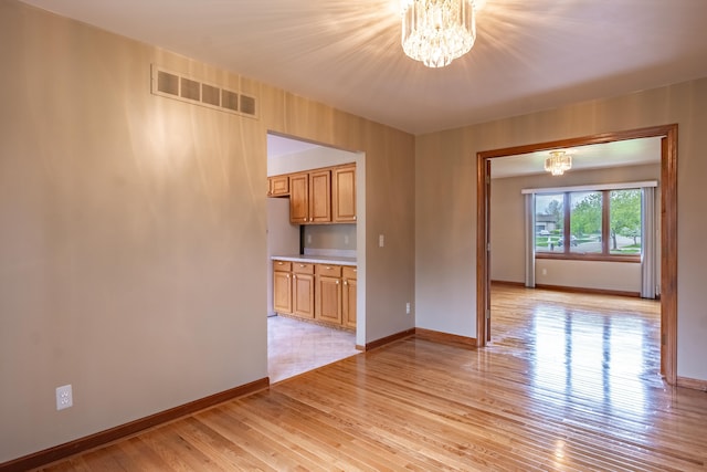 unfurnished room featuring a chandelier, baseboards, and light wood finished floors
