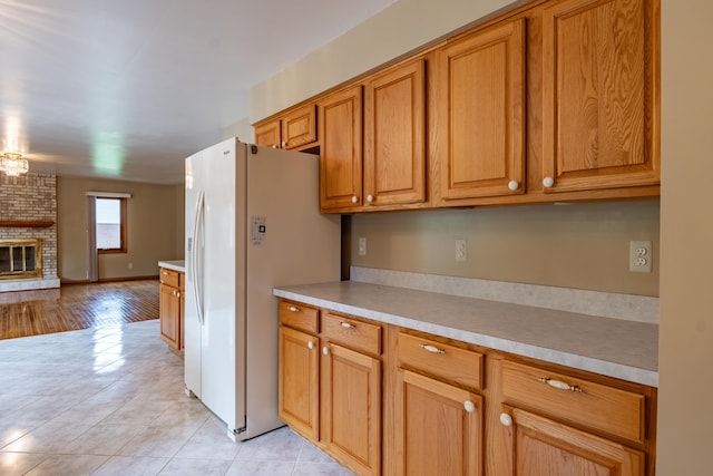kitchen with white fridge with ice dispenser, light countertops, light tile patterned floors, and brown cabinetry