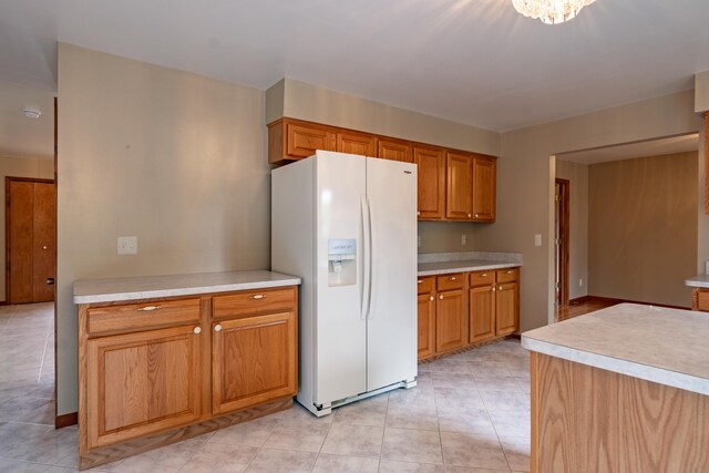 kitchen featuring white fridge with ice dispenser, light countertops, brown cabinets, and light tile patterned floors