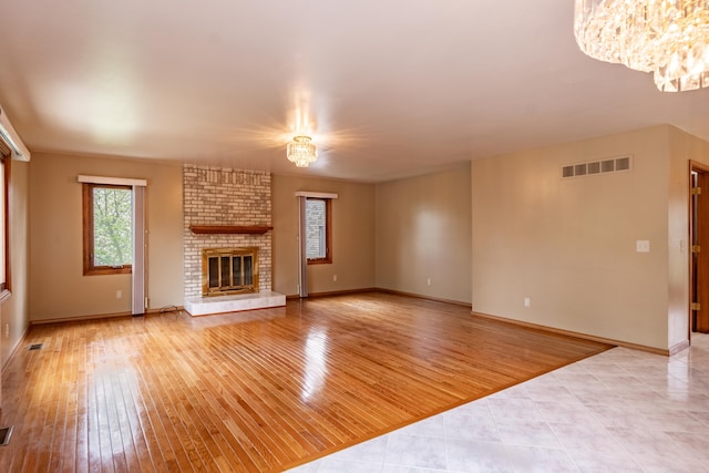 unfurnished living room with a chandelier, light wood-type flooring, a fireplace, and baseboards