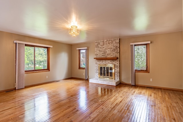 unfurnished living room with wood-type flooring, a chandelier, a brick fireplace, and baseboards