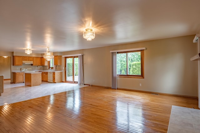unfurnished living room with a chandelier, light wood-style flooring, a sink, and baseboards