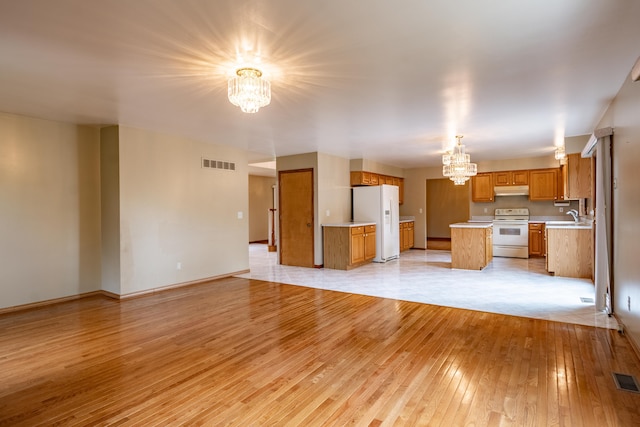 unfurnished living room with a chandelier, a sink, light wood finished floors, and baseboards