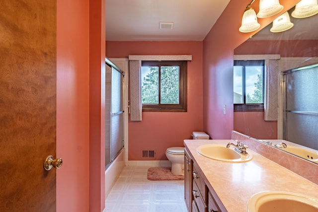 bathroom featuring double vanity, toilet, baseboards, tile patterned floors, and bath / shower combo with glass door