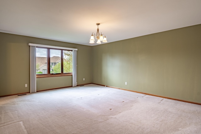spare room featuring a chandelier, light colored carpet, and baseboards