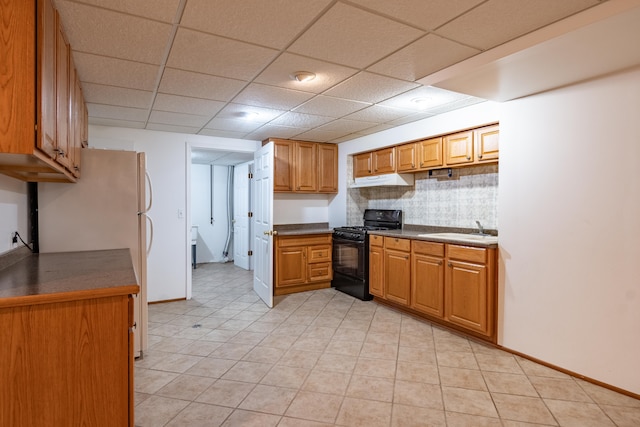 kitchen with black gas range oven, freestanding refrigerator, a sink, under cabinet range hood, and decorative backsplash