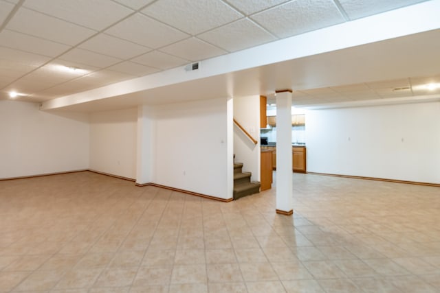 finished basement featuring a paneled ceiling, stairway, and baseboards