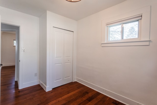 unfurnished bedroom with baseboards, dark wood-style flooring, and a closet