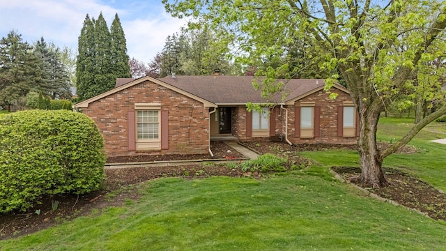 ranch-style house featuring a chimney, a front yard, roof with shingles, and brick siding