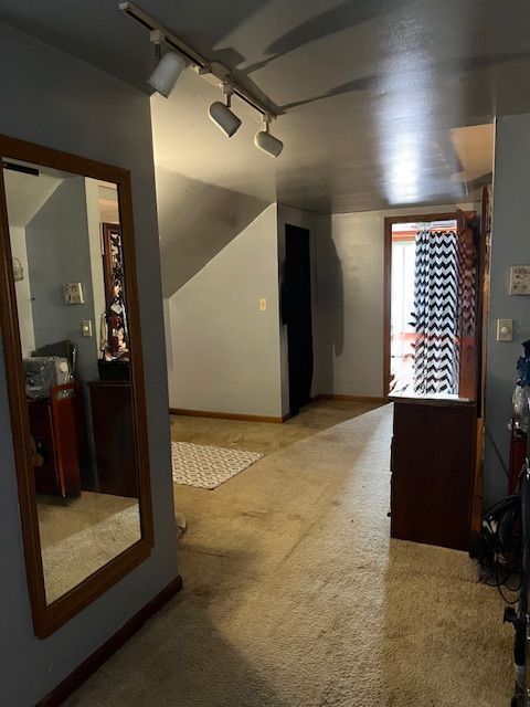 hall featuring track lighting, carpet, and baseboards