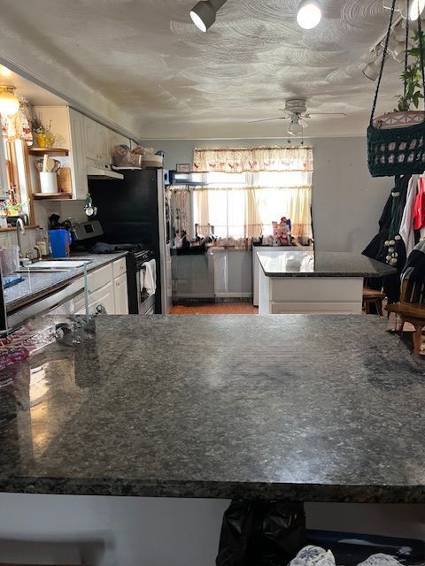kitchen with stainless steel range oven, white cabinetry, open shelves, a sink, and under cabinet range hood