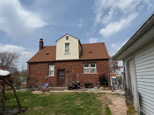 rear view of property with brick siding, a lawn, and a chimney