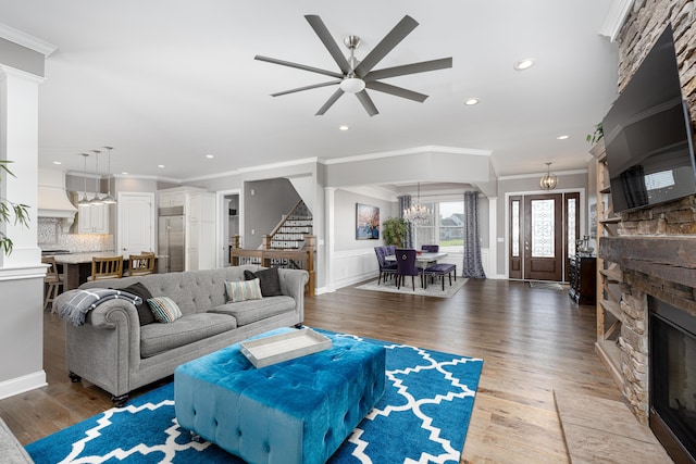 living area featuring crown molding, wood finished floors, a stone fireplace, and stairs