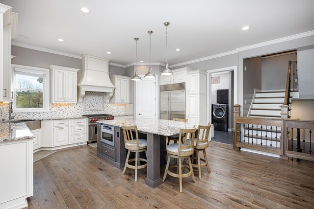 kitchen featuring washer / clothes dryer, a sink, custom range hood, high end appliances, and wood finished floors