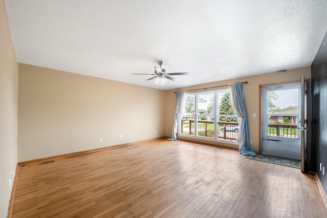 spare room with light wood finished floors, a textured ceiling, a ceiling fan, and visible vents