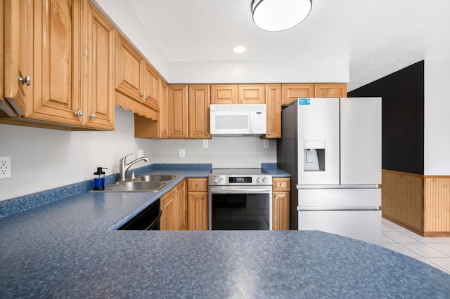 kitchen with a sink, dark countertops, a wainscoted wall, white appliances, and light tile patterned flooring