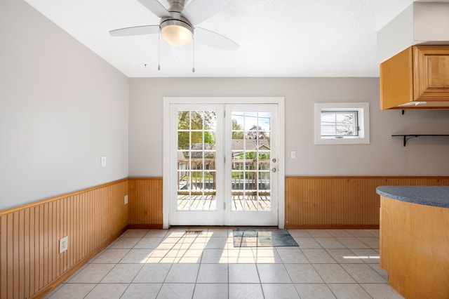 doorway to outside featuring light tile patterned flooring, a ceiling fan, wooden walls, and wainscoting