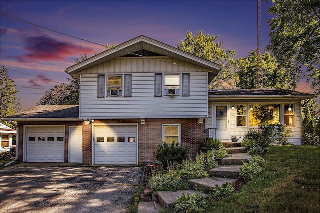 tri-level home with driveway, cooling unit, brick siding, and an attached garage