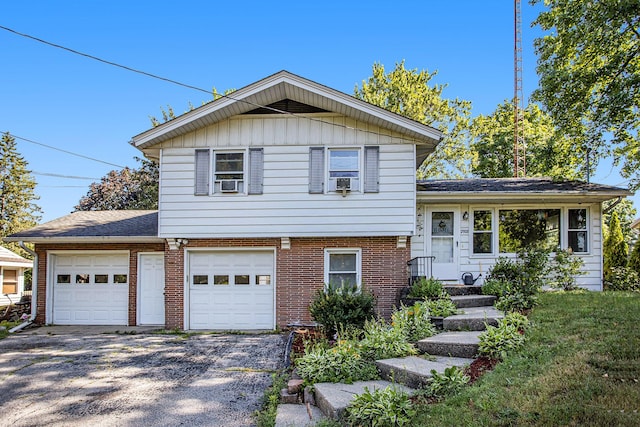 tri-level home with a garage, cooling unit, brick siding, and gravel driveway