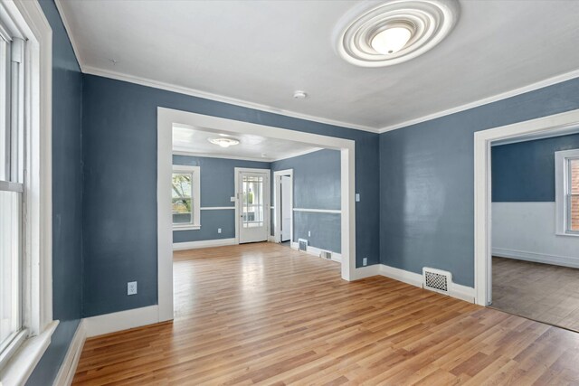 empty room featuring crown molding, baseboards, visible vents, and light wood-style floors