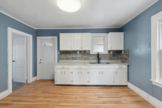 kitchen featuring light wood-style flooring, a sink, white cabinetry, light countertops, and decorative backsplash