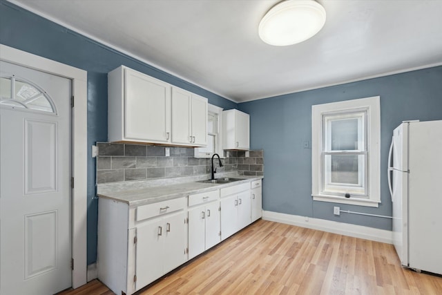 kitchen featuring freestanding refrigerator, light countertops, white cabinets, and a sink
