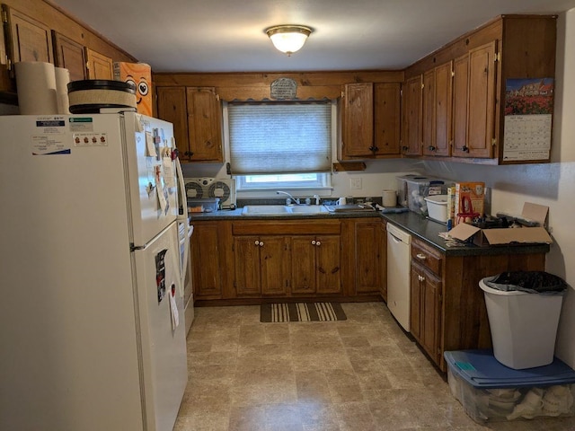 kitchen with white appliances, brown cabinetry, dark countertops, and a sink