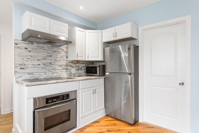 kitchen featuring tasteful backsplash, light wood-type flooring, under cabinet range hood, white cabinets, and appliances with stainless steel finishes