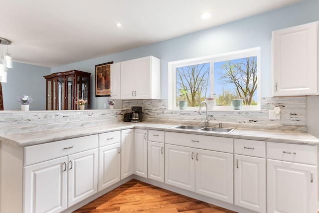 kitchen featuring a sink, a peninsula, light wood-style flooring, white cabinetry, and decorative backsplash