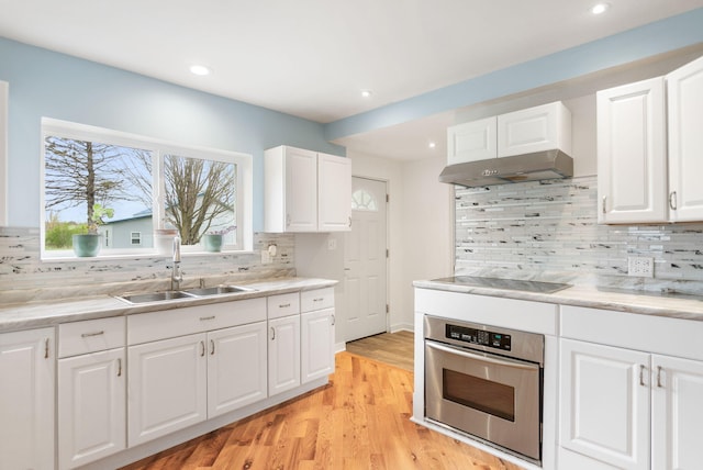 kitchen with under cabinet range hood, a sink, black electric cooktop, decorative backsplash, and stainless steel oven