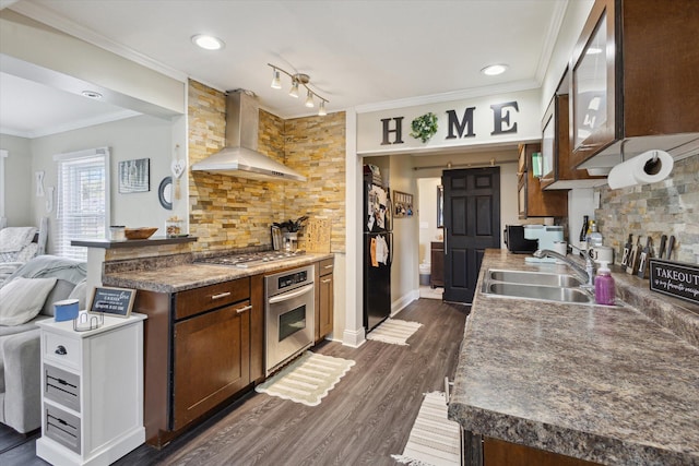 kitchen featuring a sink, wall chimney range hood, ornamental molding, black appliances, and decorative backsplash