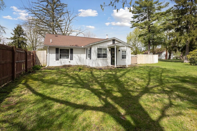 rear view of house with a lawn, roof with shingles, and fence
