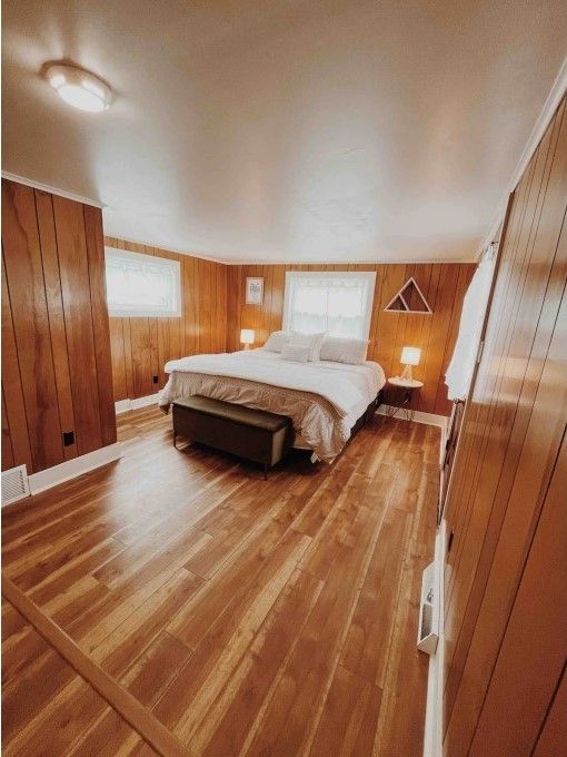 bedroom featuring wood walls, baseboards, visible vents, and wood finished floors