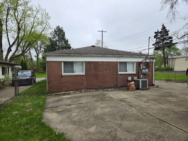view of property exterior featuring a shingled roof, brick siding, fence, and central AC
