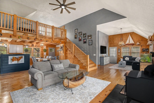living area with hardwood / wood-style flooring, wood walls, ceiling fan with notable chandelier, a textured ceiling, and a healthy amount of sunlight
