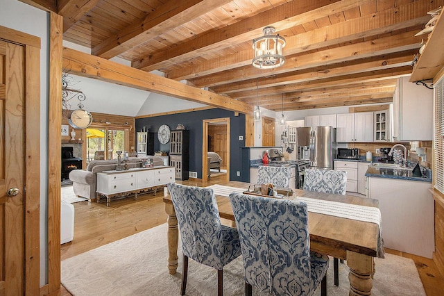 dining room with light wood finished floors, vaulted ceiling with beams, and wooden ceiling