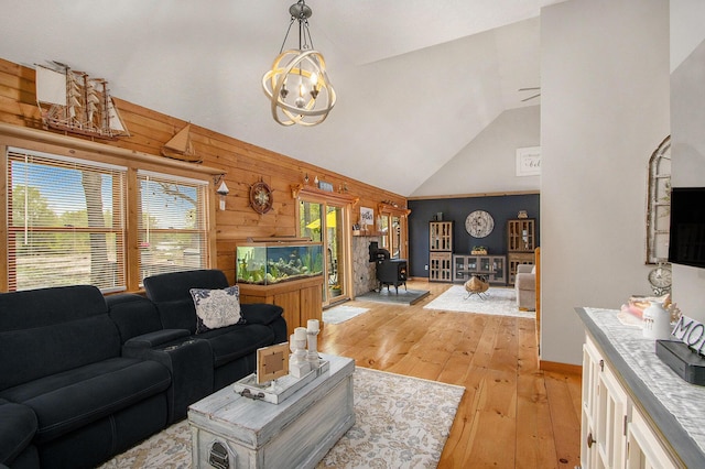 living room featuring wood walls, a wood stove, light wood-type flooring, vaulted ceiling, and a notable chandelier