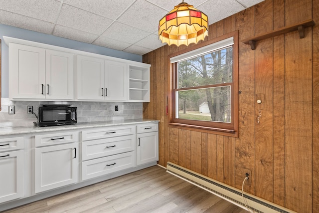 kitchen featuring backsplash, wood walls, a baseboard radiator, and black microwave