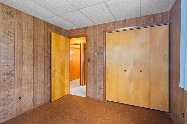 unfurnished bedroom featuring carpet flooring, a closet, wood walls, and a paneled ceiling