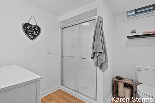 bathroom featuring toilet, wood finished floors, vanity, a shower stall, and baseboards