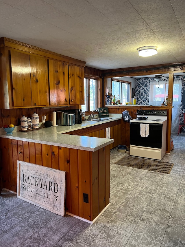 kitchen with a peninsula, brown cabinets, a sink, electric stove, and light countertops