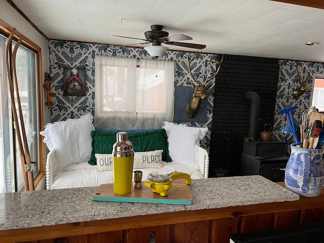 interior space featuring a wood stove, a ceiling fan, and wallpapered walls