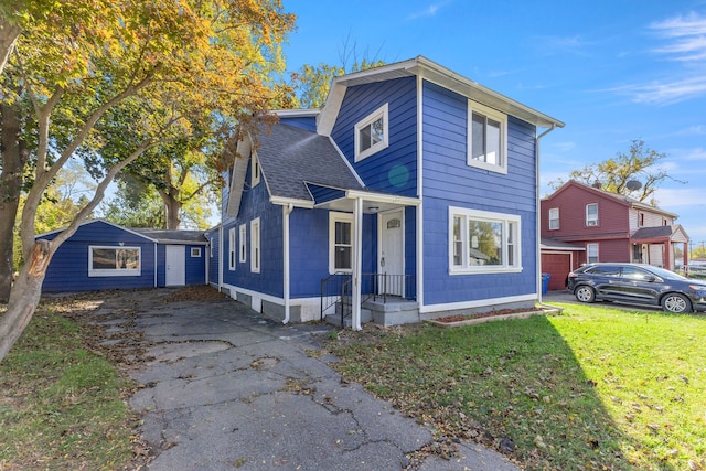 traditional home with a front lawn, a shingled roof, an outbuilding, and aphalt driveway