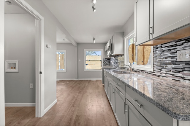kitchen with a sink, light wood-type flooring, backsplash, stone counters, and baseboards